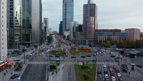 Heavy-traffic-downtown.-Forwards-fly-above-wide-multilane-road-and-large-roundabout-among-multistorey-buildings.-Warsaw,-Poland