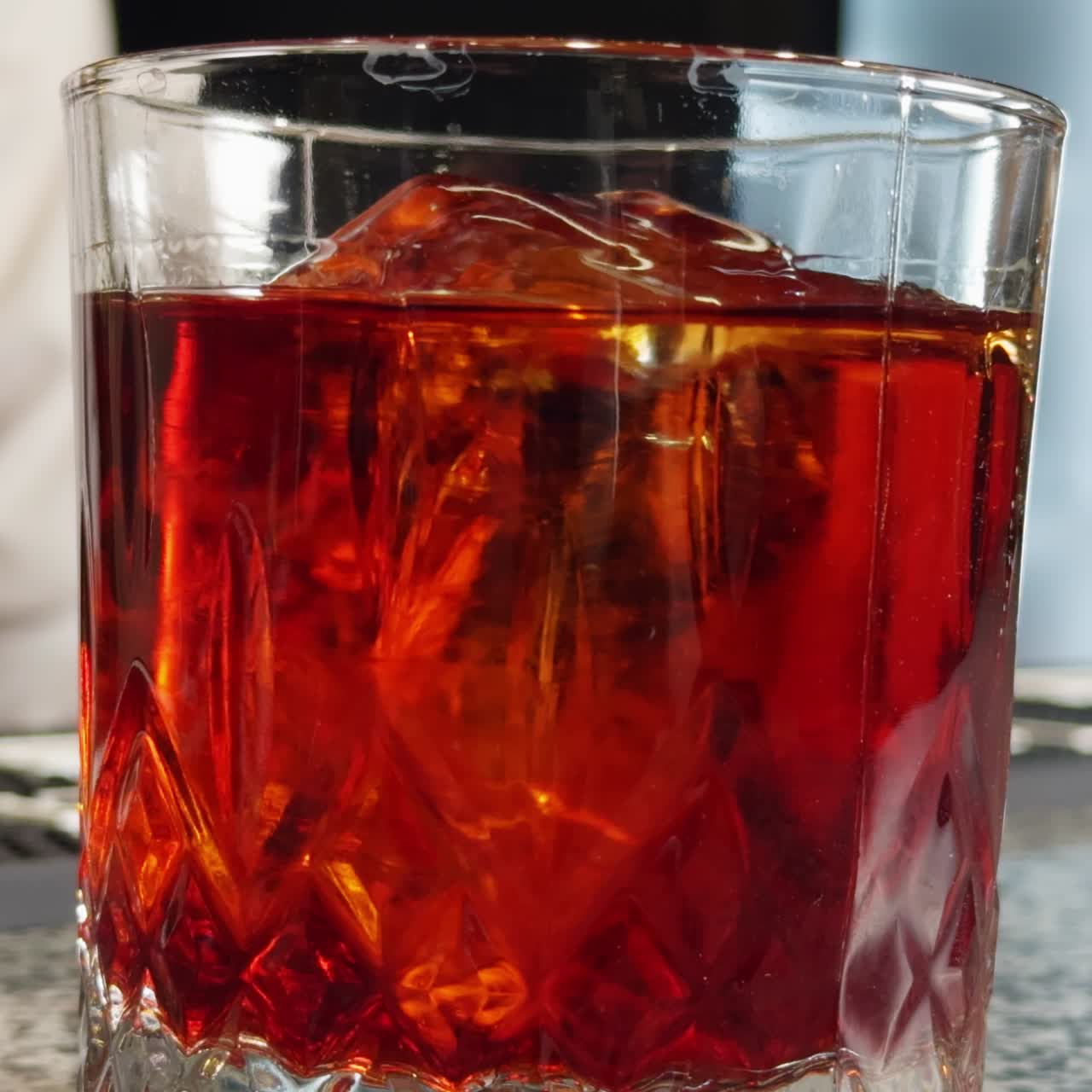 Bicchiere vecchio stile riempito con liquido arancione. Un barman uomo non riconoscibile mescola la bevanda con un cucchiaio. Primo piano. Sfondo sfocato.
