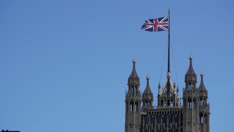 top of victoria tower, palace of westminster in london, united kingdom. union jack, flag flies on sky. square tower. perpendicular gothic stonework golden ornaments. holds parliamentary archives.
