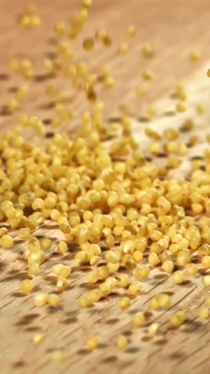 Goldene Hirsekörner fallen auf eine helle Holzoberfläche