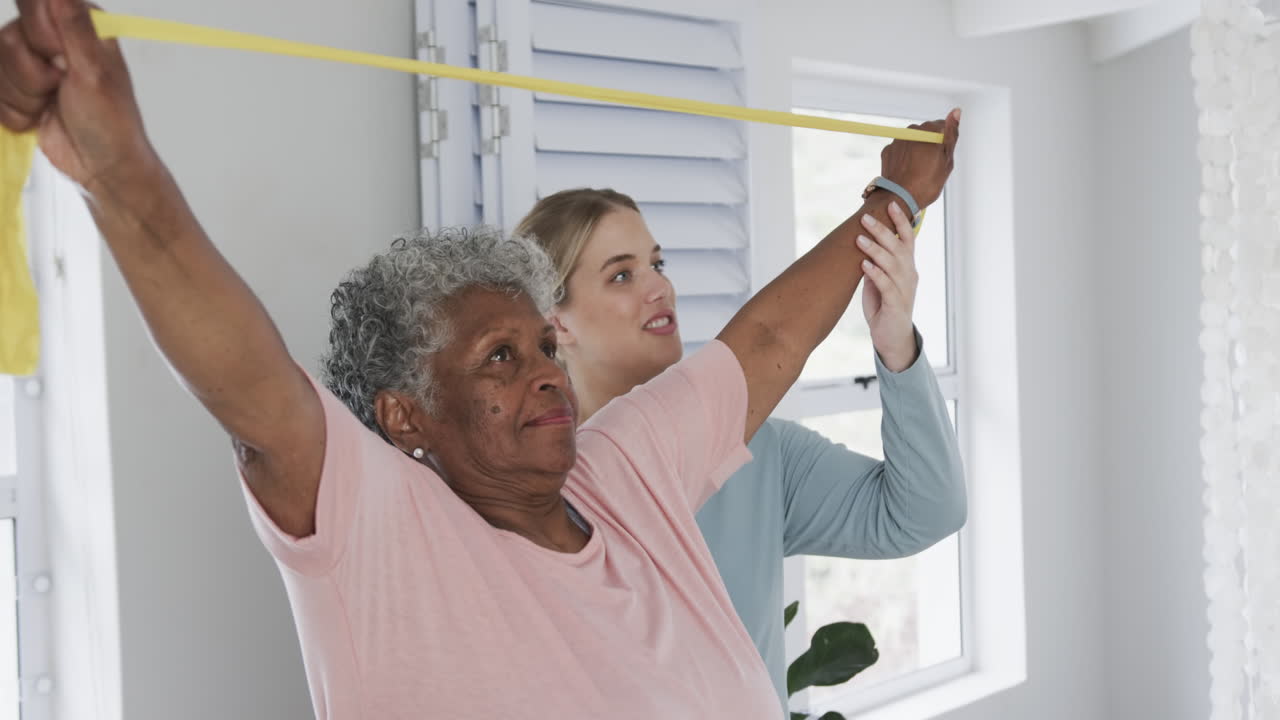 Caucasian nurse with senior woman exercising with rubber band, copy space, slow motion