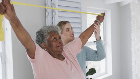 caucasian nurse with senior woman exercising with rubber band, copy space, slow motion