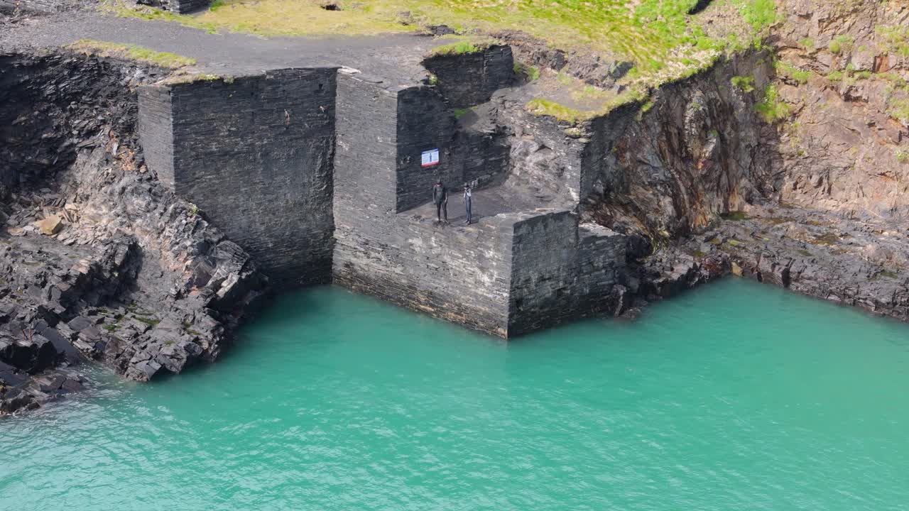 Tow men prepare to dive from abandoned quarry structure into blue lagoon water in Pembrokeshire
