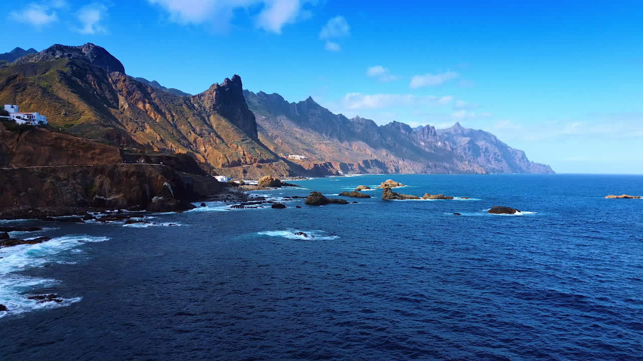 Rocks stick out of blue waterscape of the Atlantic Ocean at the coast of Tenerife, the Canary Islands, Spain. Some villas located on the rocky shore