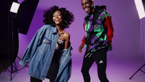 two young, stylish adults posing happily in a vibrant purple studio
