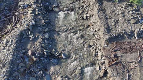 Drone footage captures a rocky glacial stream with clear water flowing amidst stones and driftwood in natural light