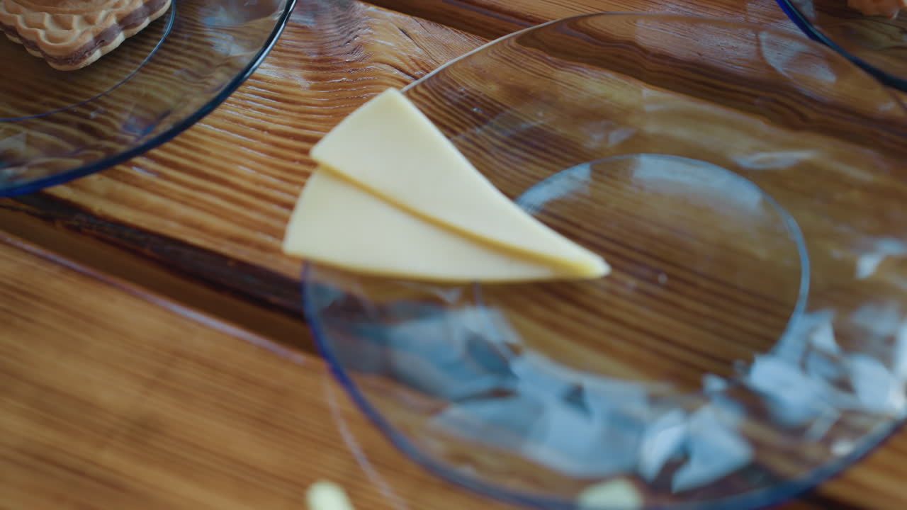 Two triangular cheese slices neatly arranged on transparent glass plate set atop smooth wooden table, reflecting warm light and subtle surface textures
