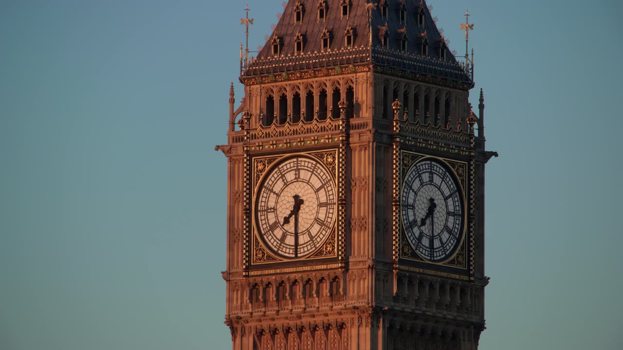 Closeup of Big Ben’s ornate clock faces glows in golden sunset light against a clear sky, highlighting beautiful stonework on London’s most famous landmark