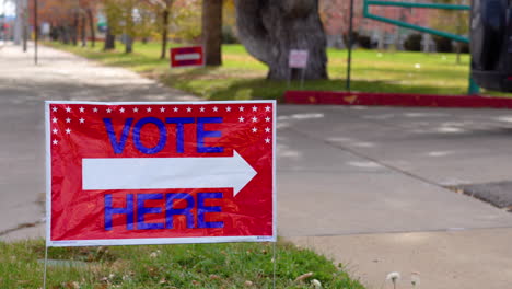 vote here signs pointing right with a person driving a car in background, close up