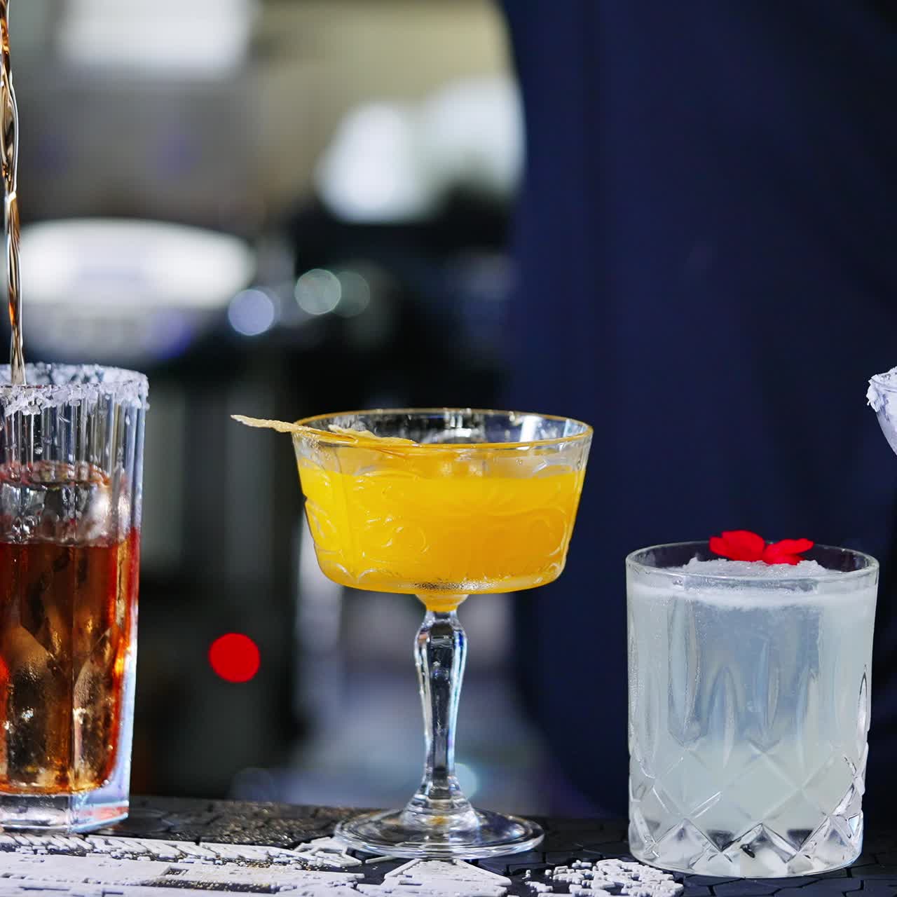 Beautiful tasty cocktails in diverse glasses. Barman in black shirt pours red beverage into a glass with salt on top. Close up