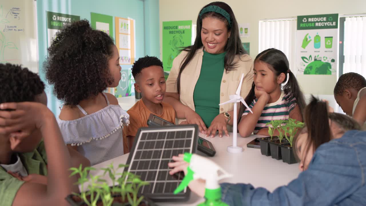 Teacher with students showing tilted solar panel at table, children touching plants learning energy