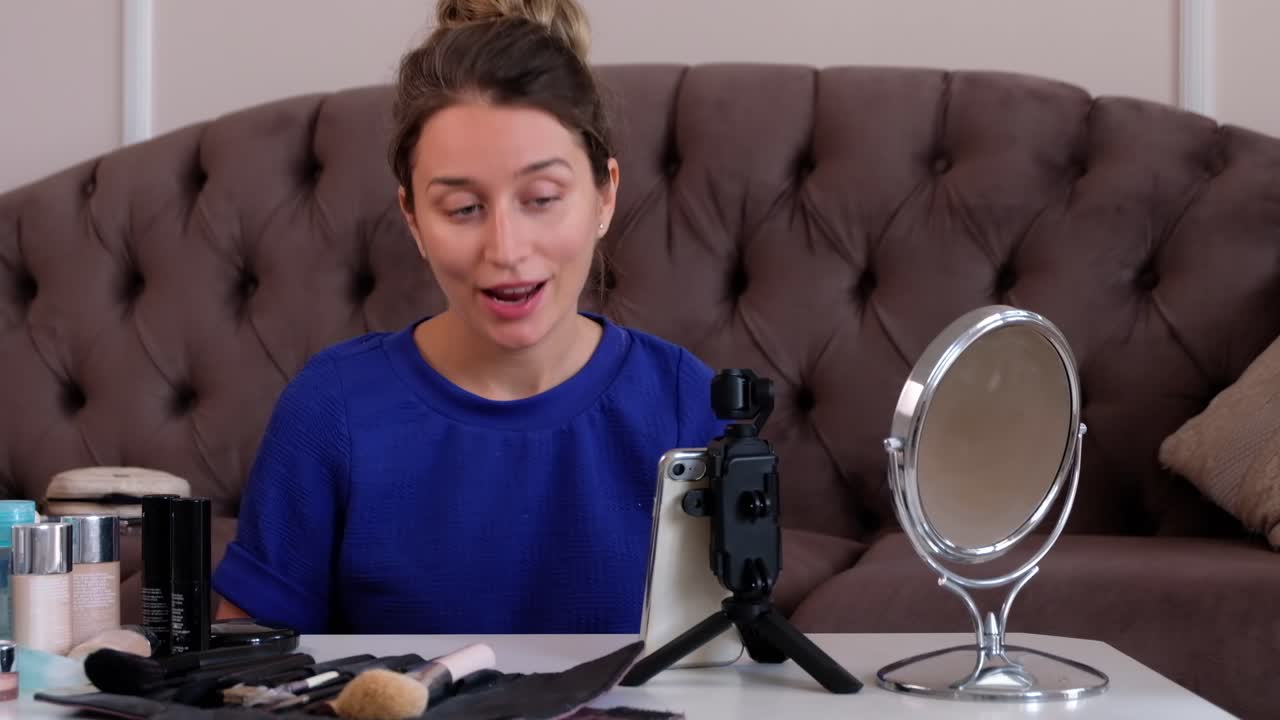 Woman in a blue T-shirt filming herself while doing a make-up tutorial at home