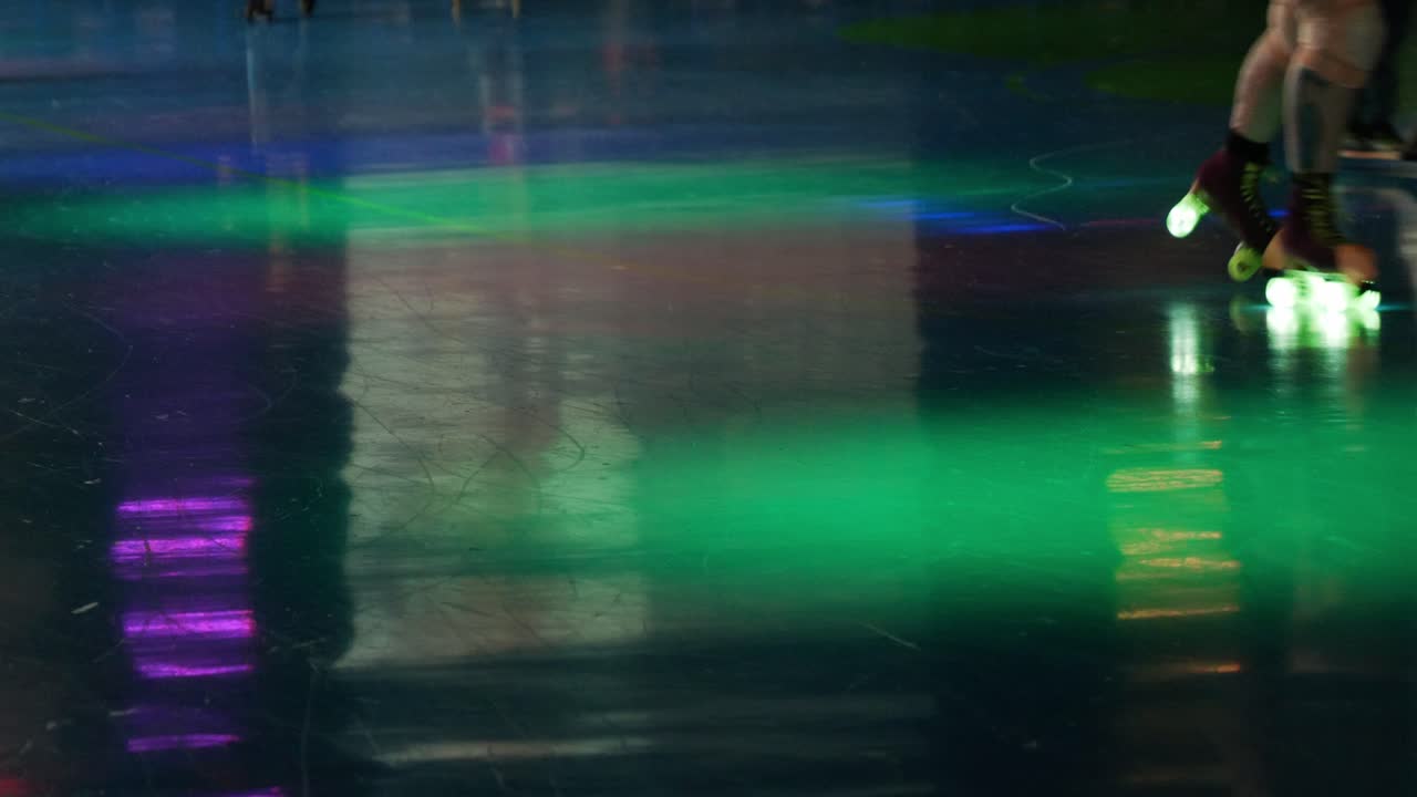 Busy roller skating rink with razor scooters rollerblades and rollerskates on people as they skate around brightly colored darkly lit venue - in Cinema 4k (30fps slowed from 60fps).