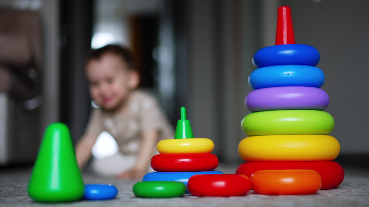 Smaller and bigger pyramid on the floor. Kid comes up to toys but then walks away. Blurred backdrop.