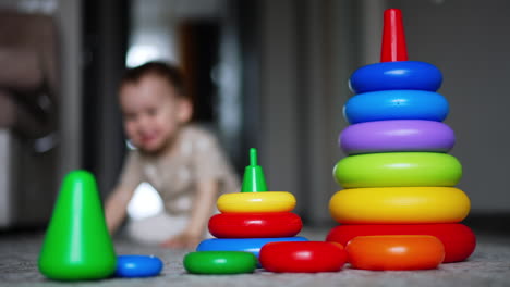 smaller and bigger pyramid on the floor. kid comes up to toys but then walks away. blurred backdrop.