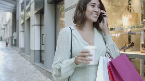 señora latina caminando cerca de las tiendas, hablando por teléfono inteligente