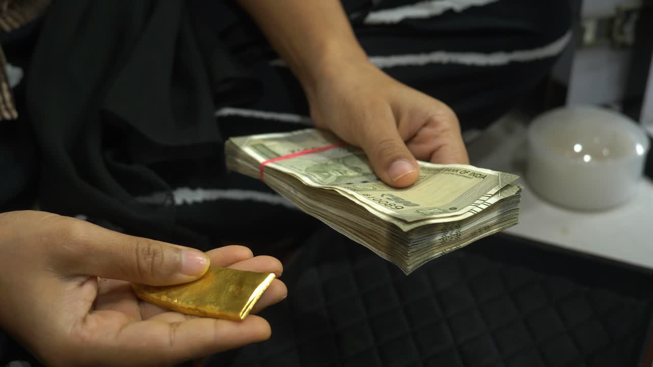 Hands comparing 24k raw gold and Indian rupee banknotes for gold investment