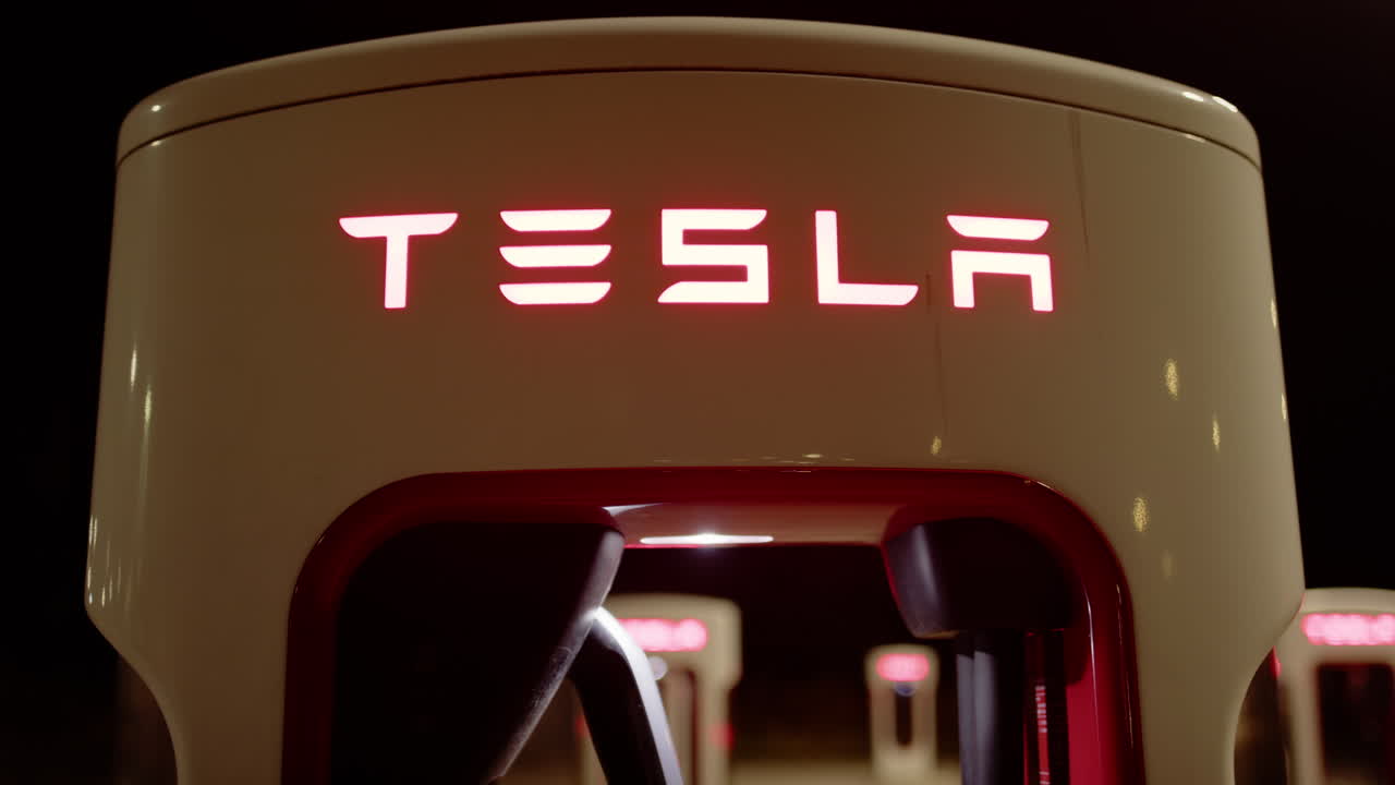 Close tilt-up reveal shot of red illuminated Tesla Supercharger charging station
