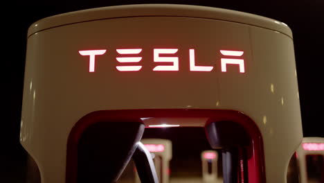 close tilt-up reveal shot of red illuminated tesla supercharger charging station