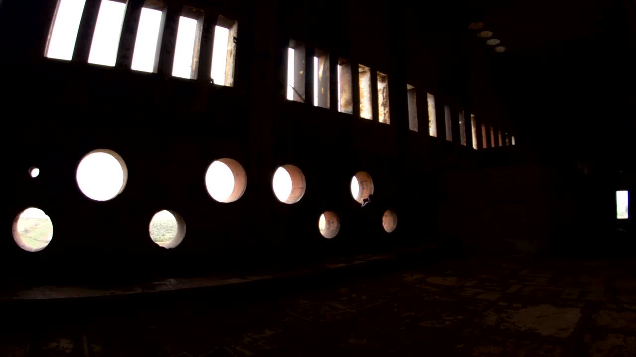 a woman takes a photograph through a round window in an abandoned building