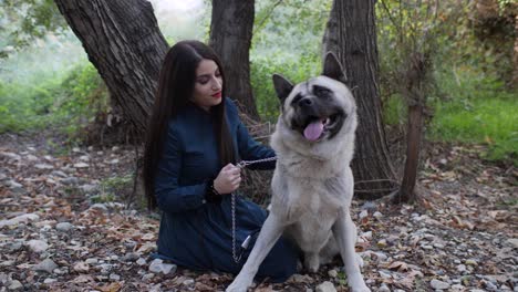 Eine-Frau-Und-Ihr-Hund-Sitzen-Im-Wald,-Während-Sie-Liebevoll-Ihren-Glücklichen-Akita-Streichelt