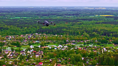 black civilian drone flying above town surrounded by forest and farmland during spring