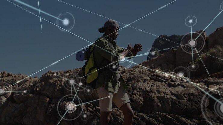 Male hiker standing on rocky outcrop, checking smartwatch showing digital network nodes for tech