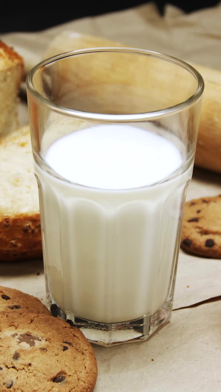 Glass of fresh milk rotating surrounded by cookies and bread in vertical composition