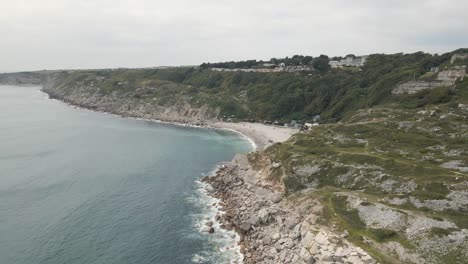 Aerial-shot-of-a-drone-moving-away-from-the-beach-of-Church-Ope,-on-the-island-of-Portland,-Dorset-UK,-flying-over-the-ocean