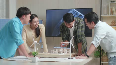 아시아 엔지니어 그룹이 사무실에서 태양 전지판이 있는 작은 집의 모형을 조립하는 것을 축하하고 있습니다.