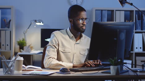 portrait of man working on the laptop turning his head to the camera and smiling in the office at night