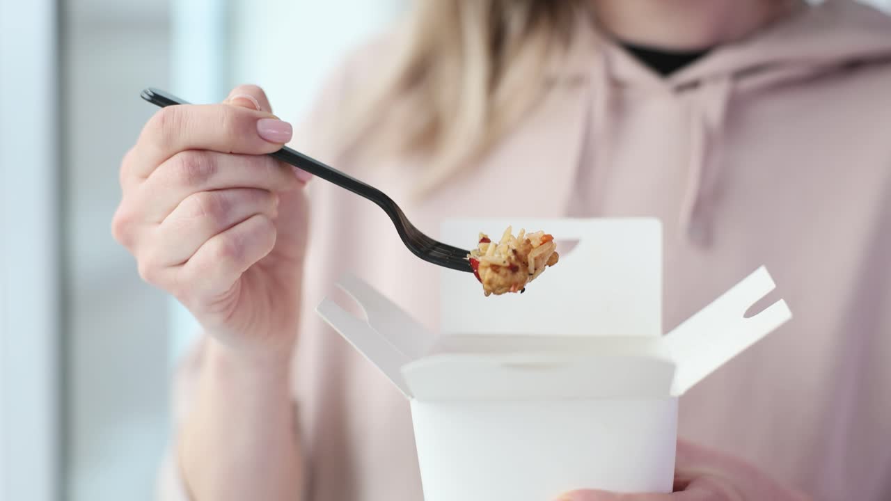 A person eating takeout food with a fork from a white box