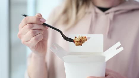 a person eating takeout food with a fork from a white box