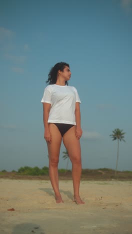 young woman standing on beach with a white t-shirt and black bikini, calm vibe