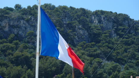 Nahaufnahme-Der-Französischen-Flagge,-Die-An-Einem-Sonnigen-Sommertag-Im-Wind-Weht,-Im-Hintergrund-Eine-Berglandschaft