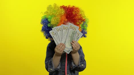 Child-girl-clown-in-colorful-wig-making-silly-faces-with-money-banknotes-dollar-cash.-Halloween