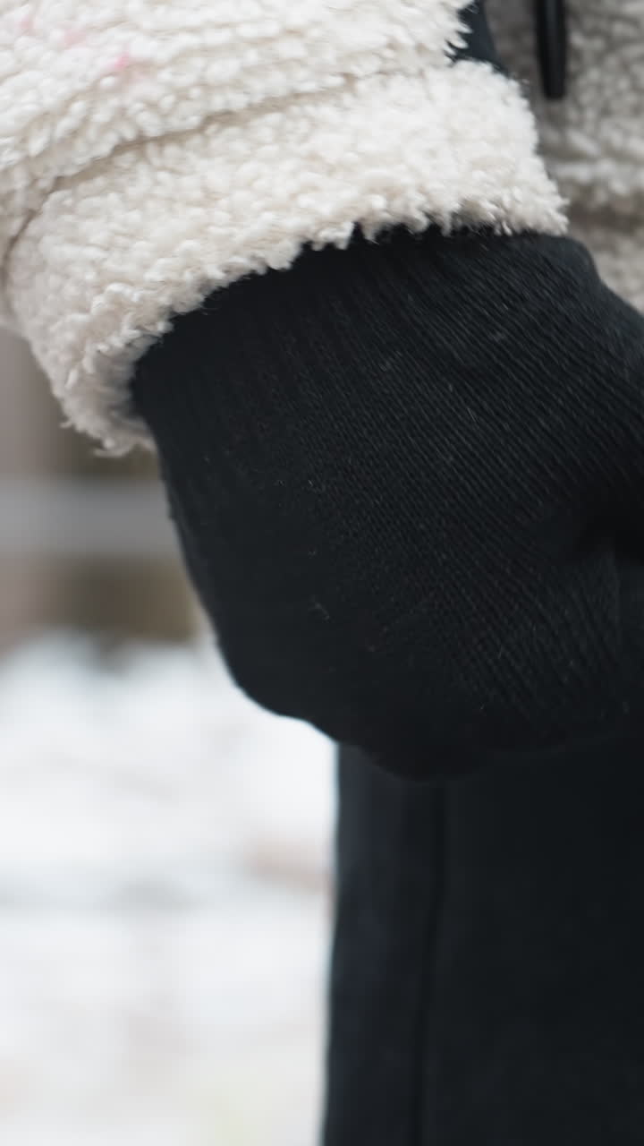 primer plano de una persona con guantes negros, chaqueta de invierno y pantalones negros realizando una torsión de muñeca, suelo cubierto de nieve y equipo de entrenamiento de madera en el fondo