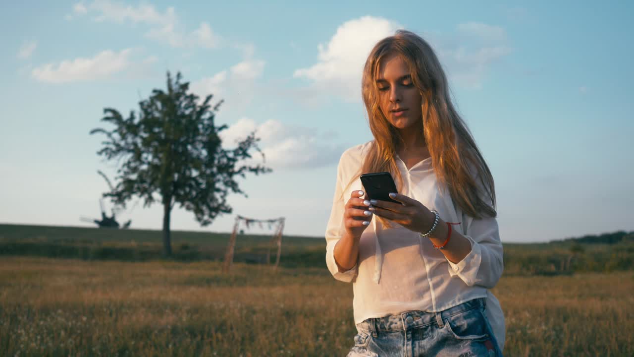 Kvinne i sommerparken bruker mobiltelefon. Autentisk kreativt bilde.