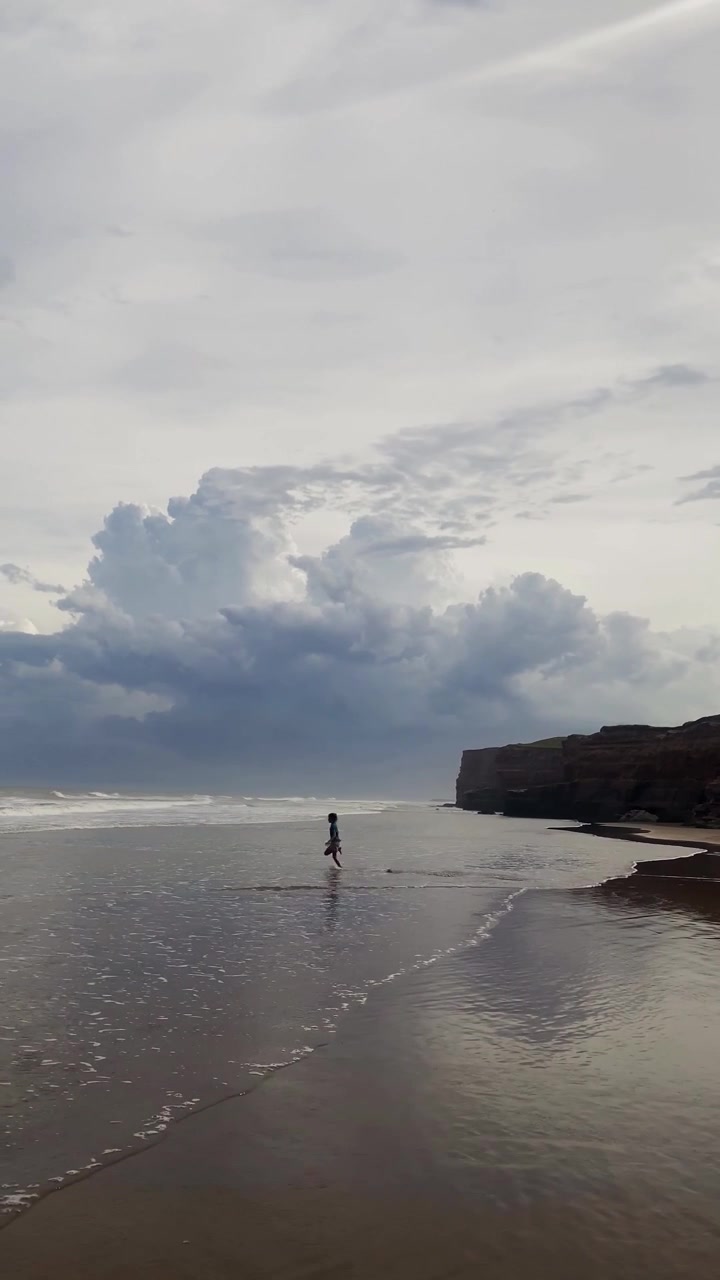 Uomo che corre sulla sabbia bagnata sulla spiaggia di Durdle Door mentre le onde si infrangono lungo la riva sotto nuvole drammatiche e scogliere frastagliate sulla Jurassic Coast, Inghilterra, Regno Unito
