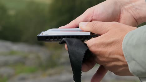 man cleaning harmonica in nature forest, close up