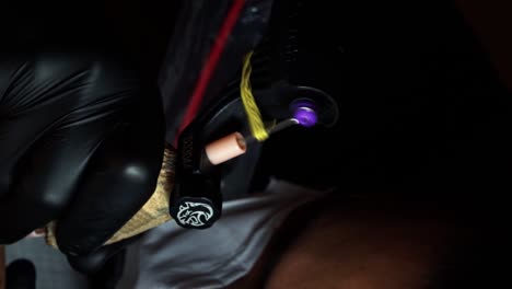 close up slow motion vertical handheld shot of a tattoo gun motor spinning as an artist works with a client in a dark tattooing studio room