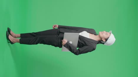 full body side view of smiling asian female engineer with laptop looking around and shaking her head in the green screen studio