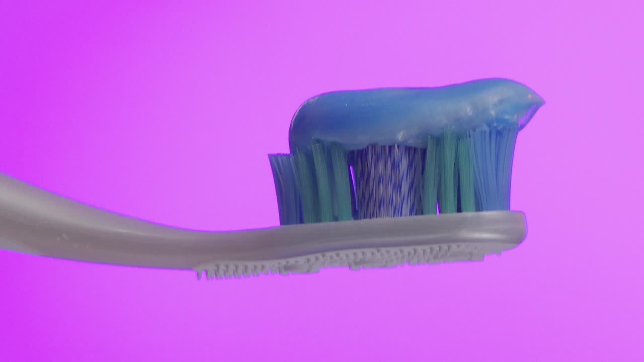 cepillo de dientes blanco con pasta de dientes azul y fondo rosa.