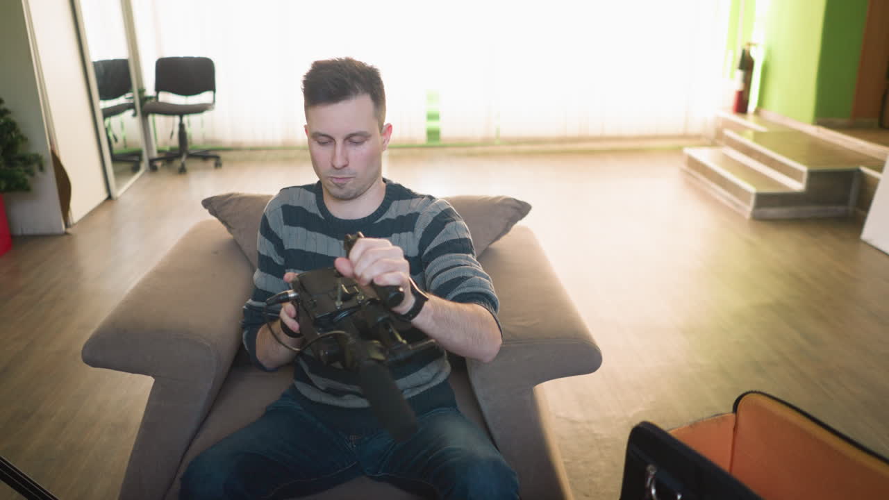 Man adjusting camera on tripod with microphone in home studio, focusing on settings. Green walls and clock in background, preparing for video production work. Indoor workspace setup