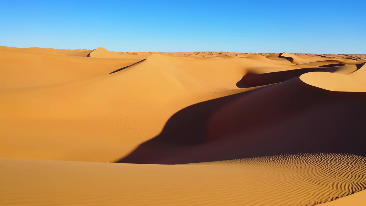 Paesaggio desertico illuminato dal sole si muove dolcemente attraverso l'inquadratura, rivelando creste di dune stratificate, profonde conche in ombra, sabbia arancione calda e delicati motivi a increspatura in primo piano