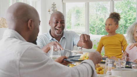 Abuelo-Tallando-Como-Familia-De-Varias-Generaciones-Sentarse-Alrededor-De-La-Mesa-En-Casa-Y-Disfrutar-De-La-Comida