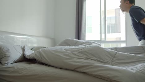 Asian-man-making-the-bed-in-his-condo-in-the-morning-with-sunshine-coming-in-the-window---slow-motion