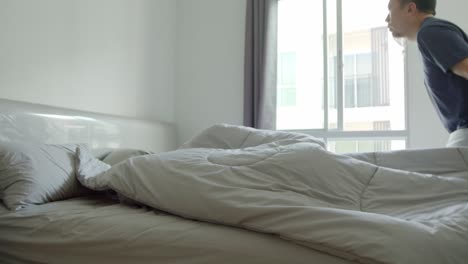 asian man making the bed in his condo in the morning with sunshine coming in the window - slow motion