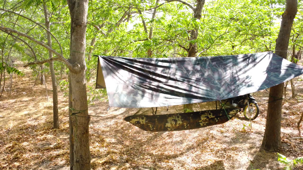 열대 지방에서 오토바이 여행을 하는 동안 태양과 비로부터 보호하는 방수포를 사용하여 숲에서 야생 캠핑을 하는 경향과 해먹 부시