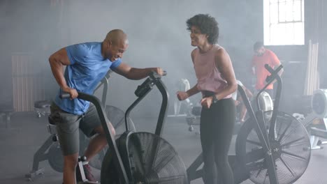 entrenadora diversa motivando a un hombre determinado entrenando duro en bicicleta elíptica en el gimnasio, cámara lenta